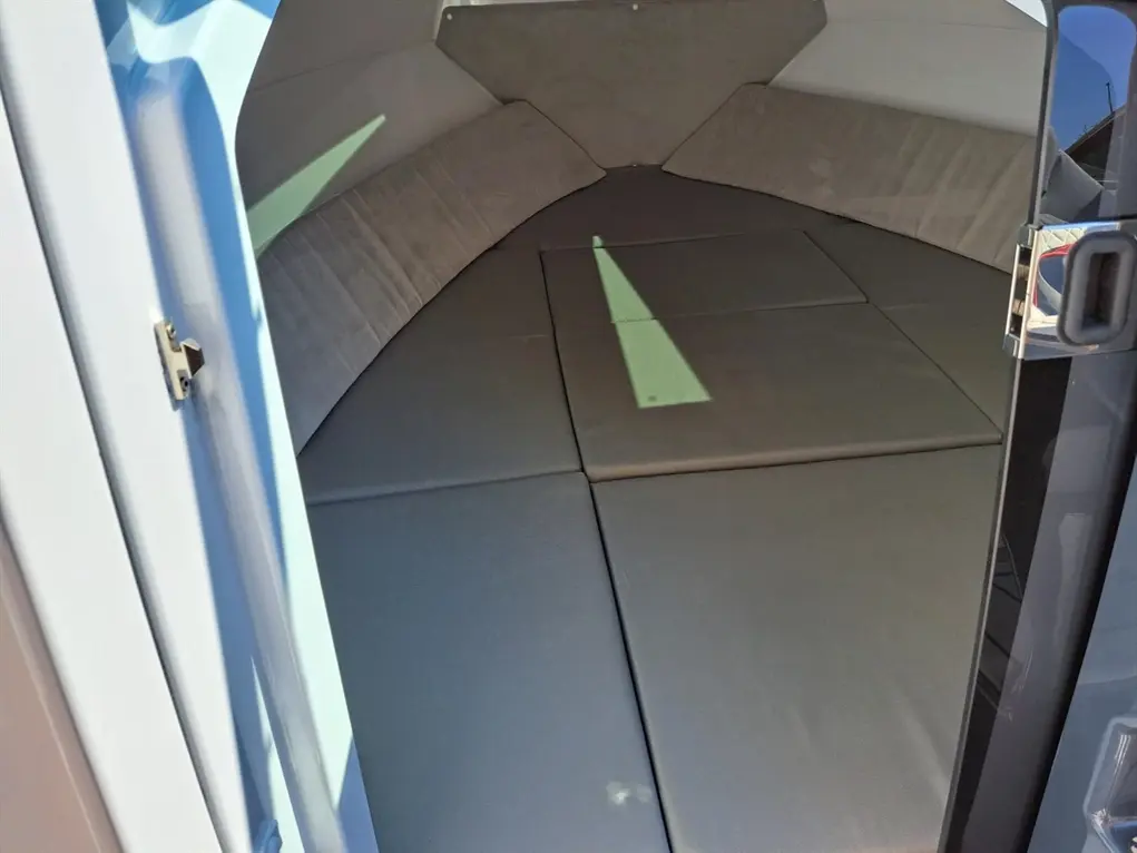 Interior view of a sleek, modern boat with grey cushioned seating and a large entrance, showcasing a minimalistic design.